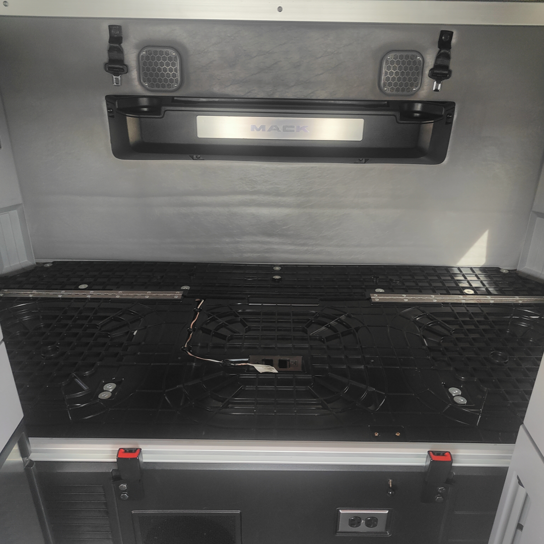 Mack AN64T70 truck bed area showing storage hatch, ventilation grills, and ventilation latches with a the Mack badge in a recessed frame.