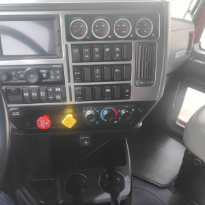 Dashboard of a Mack truck cab showing instrument gauges, control switches, climate controls, and cup holders; visible text includes gear selector letters R N D P, and various switch labels.
