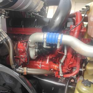 Mack AN64T70 engine bay showing turbocharger piping and blue silicone hose, red engine block, silver exhaust/intake headers, and various hoses.