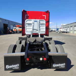 Rear view of 2022 Mack AN64T70 sleeper cab truck chassis showing dual rear axles, red cab, and Bruckner’s mud flaps with logos.