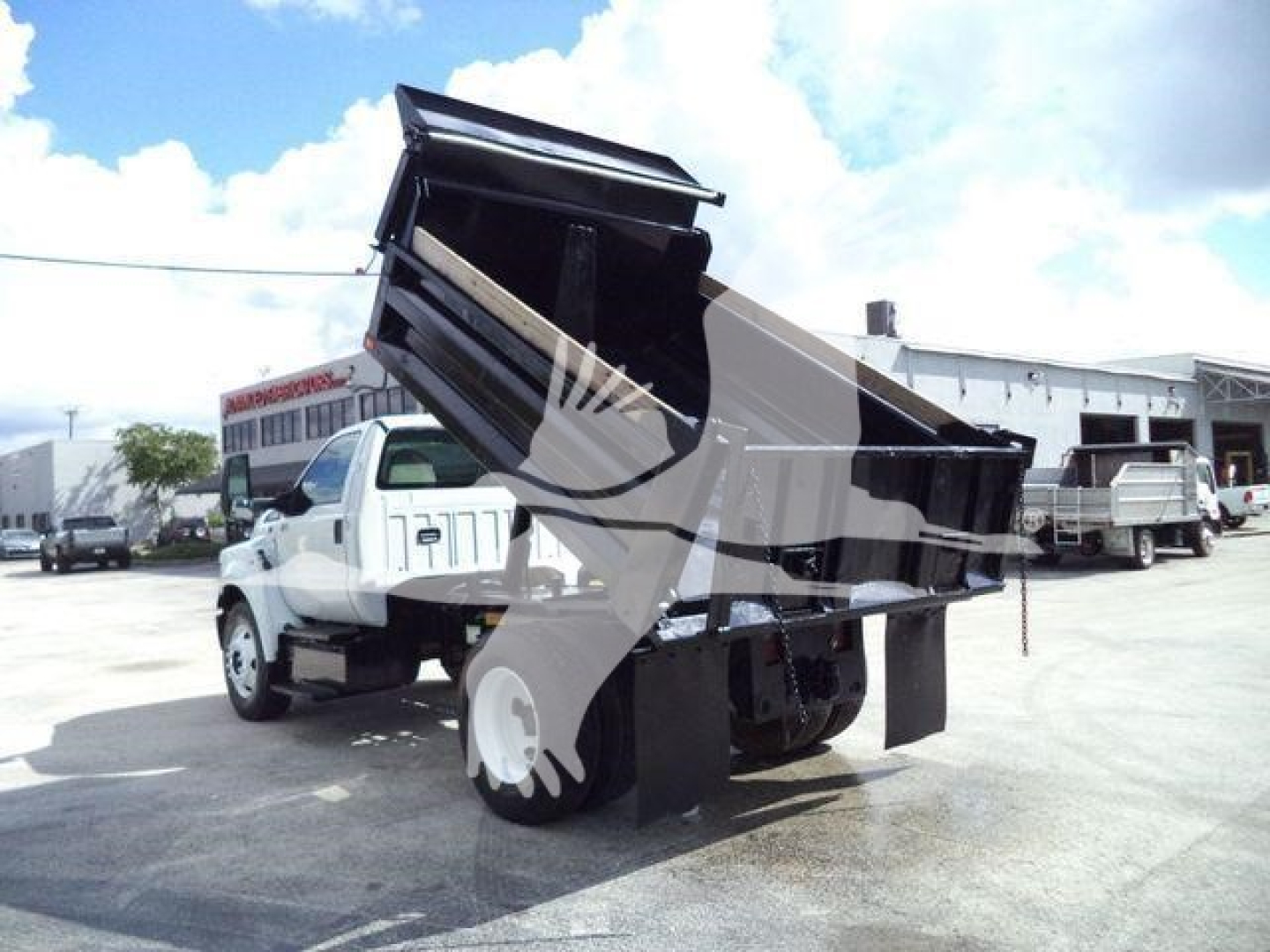 Ford F650 XL SD dump truck with lifted bed in a dealership lot, white cab, black dump body, other trucks in background.