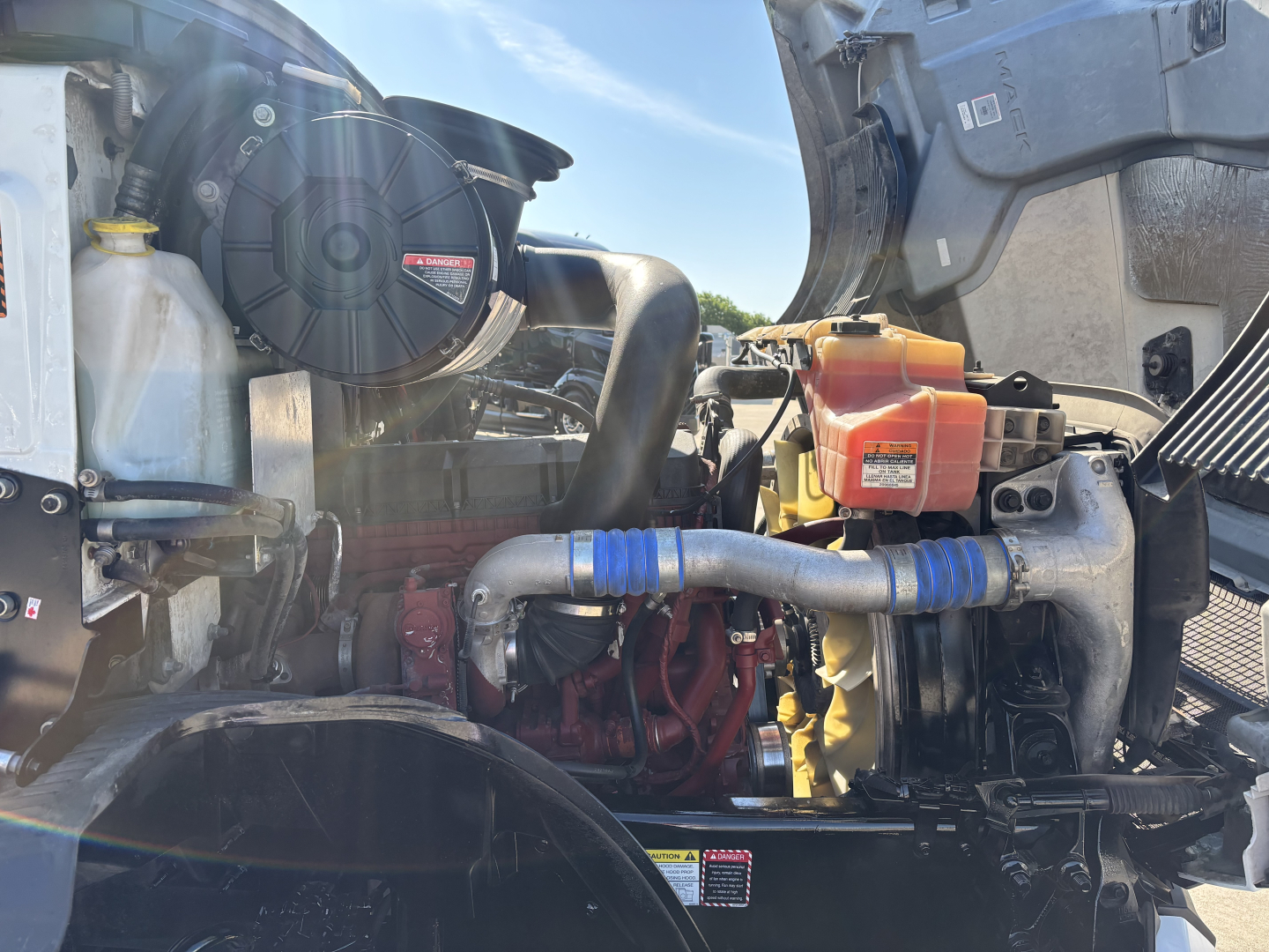 Engine bay of a 2022 Mack AN42T daycab showing engine components, hoses, and coolant reservoir.