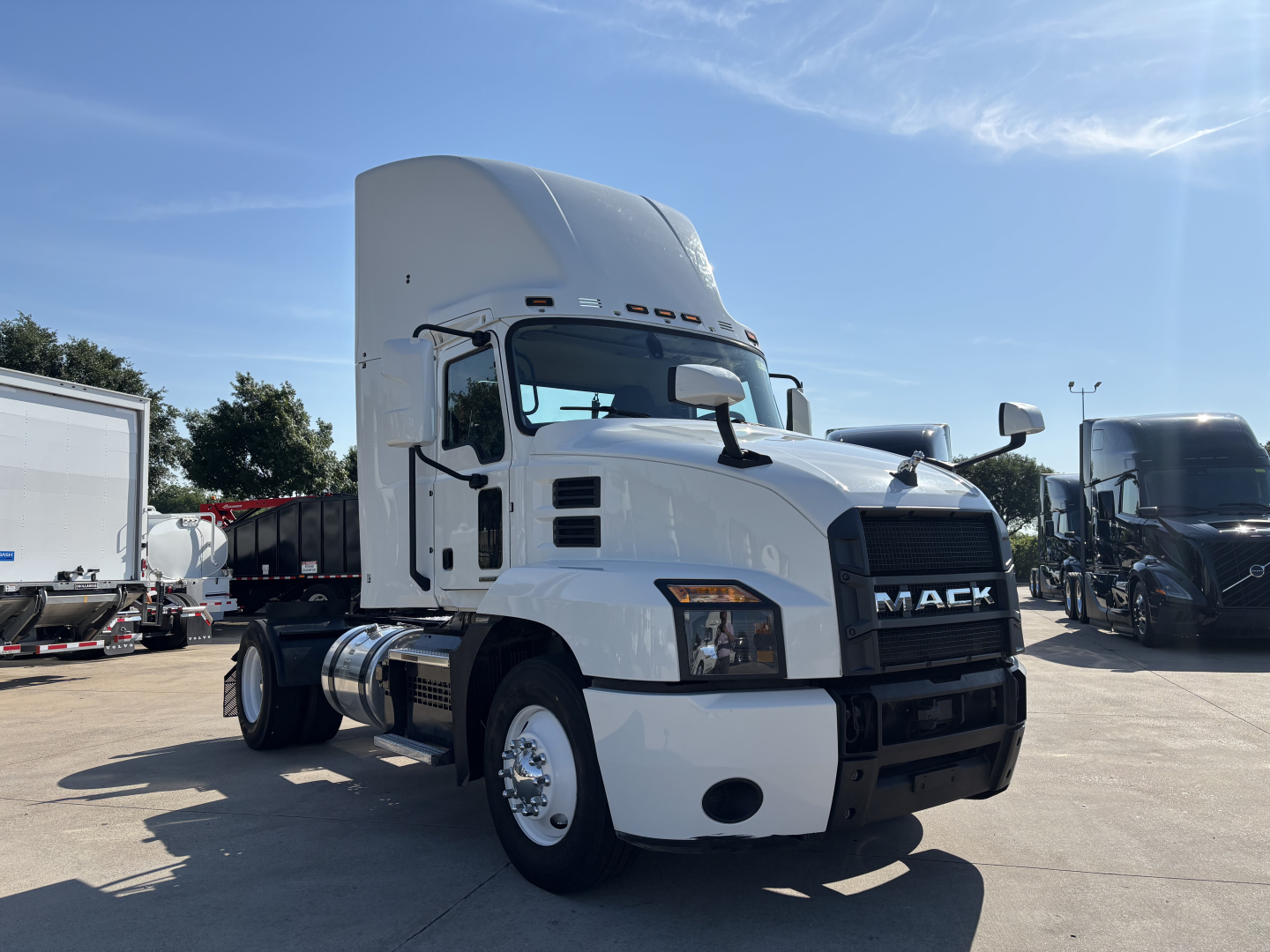 Mack AN42T conventional daycab truck in a dealership lot, white cab, large aerodynamic sleeper, front grille with Mack lettering, chrome front bumper, diesel fuel tanks