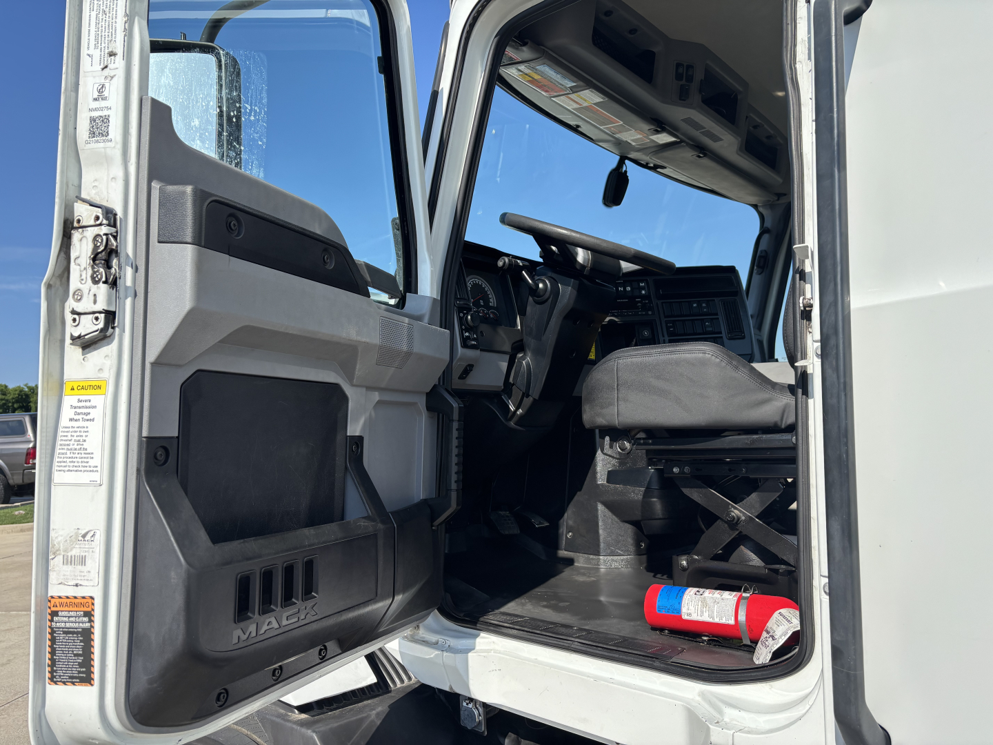 Mack AN42T truck cab interior showing driver seat and dashboard area with open door; visible steering wheel and pedals.