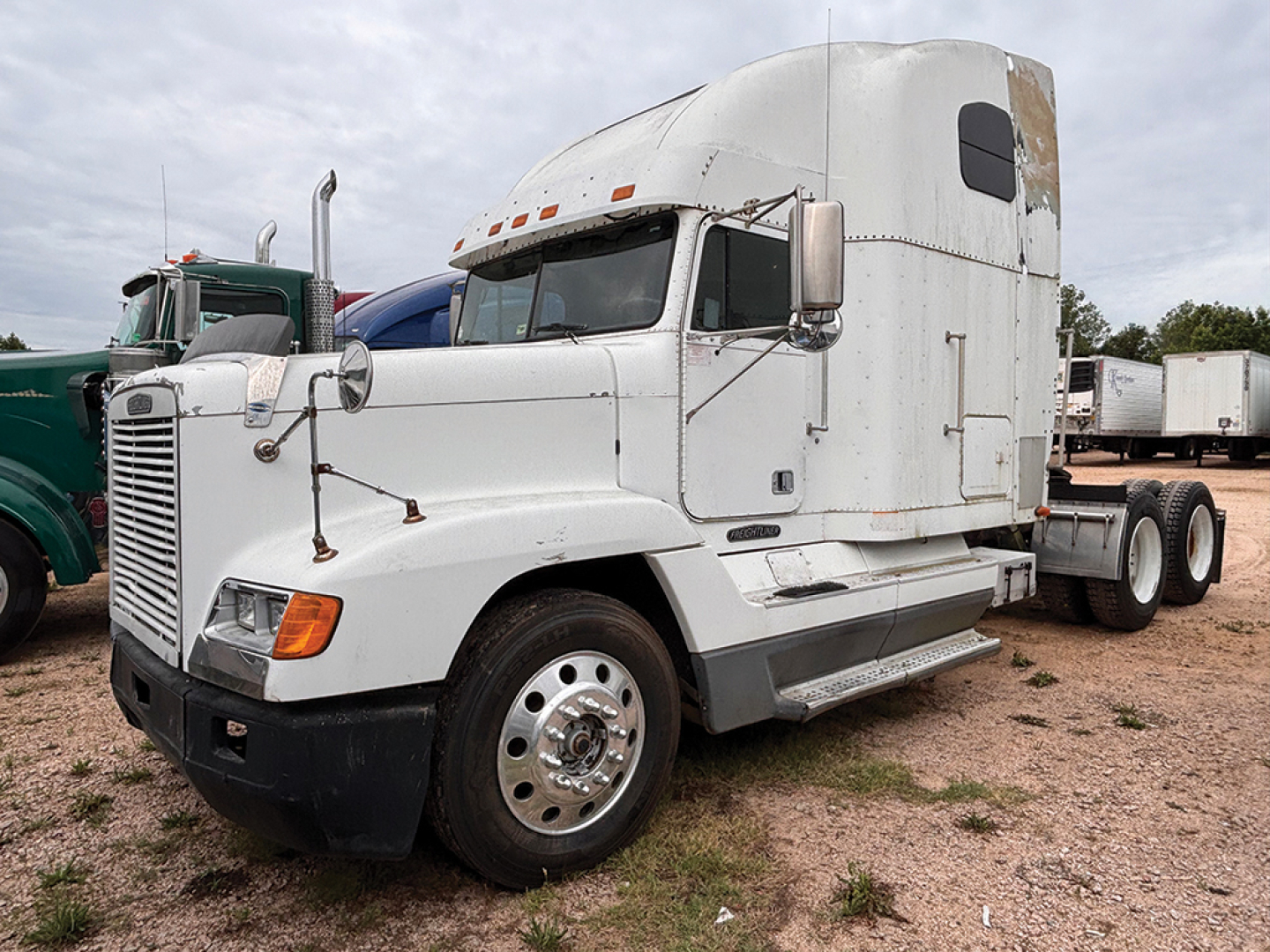 Truck cab in view showing Freightliner FLD120 sleeper with white paint and chrome wheels.