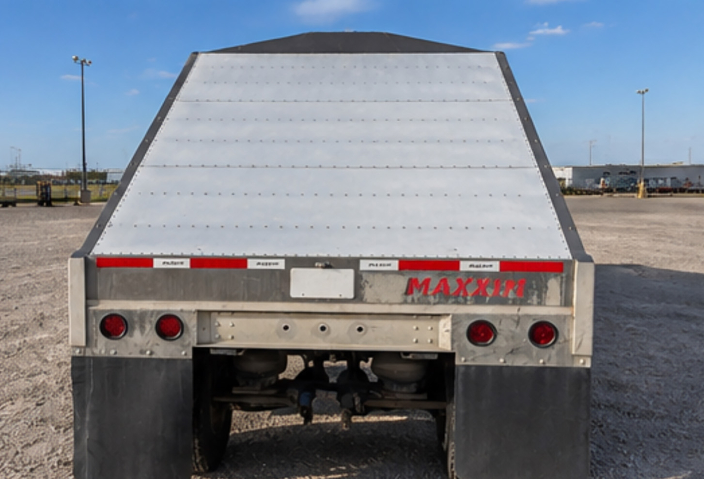 Back view of MAXXIM SAND HOPPER trailer showing aluminum rear ramp, MAXXIM logo, taillights, and hitch area.