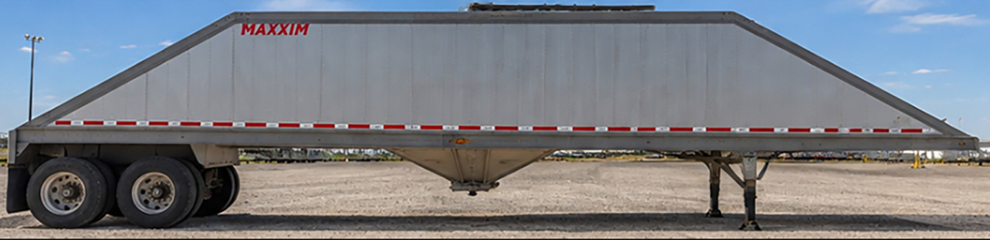 Trailer side view showing MAXXIM sand hopper trailer with dual rear axles and lowered hopper in gray color.