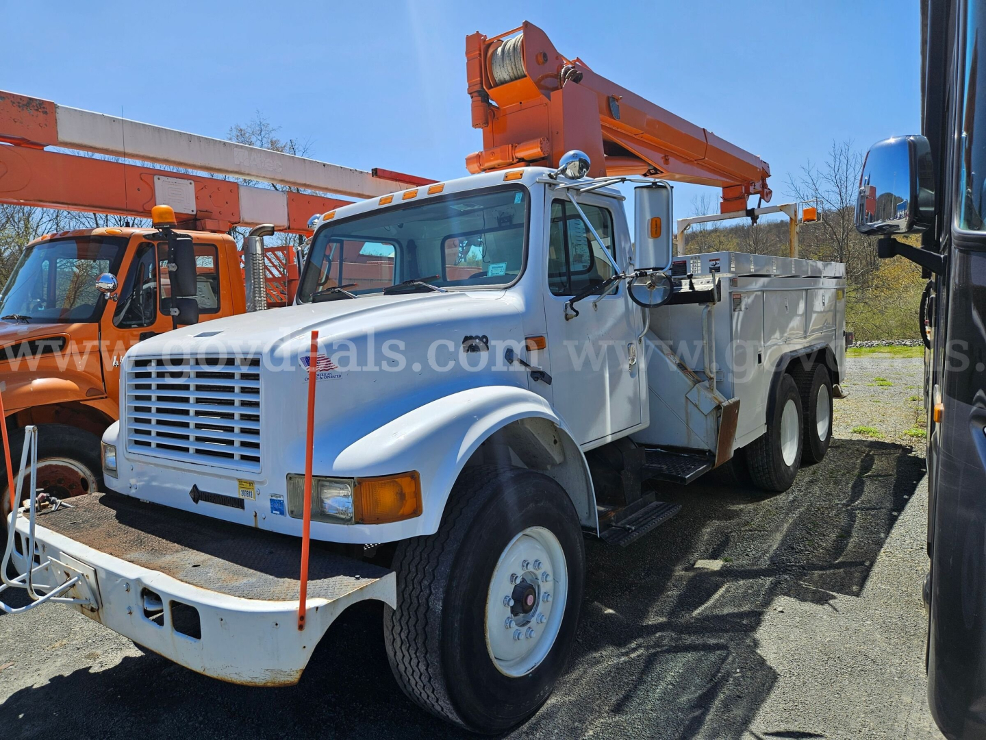 1995 International 4900 boom truck in a parking lot, front-left view showing white cab, large grille, orange boom crane, utility bed, and dual rear wheels.