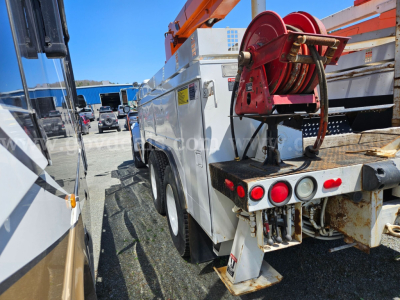 Boom truck rear view showing reel and hydraulic hose on a work truck with white body and rust on rear frame.