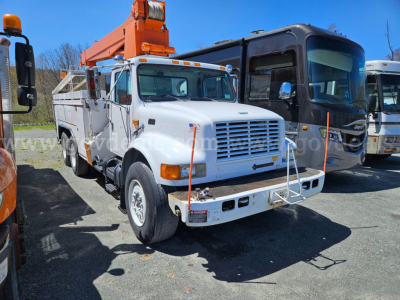 Truck front-left view of a white 1995 International 4900 boom truck with an orange crane on the bed, parked next to a black coach bus.