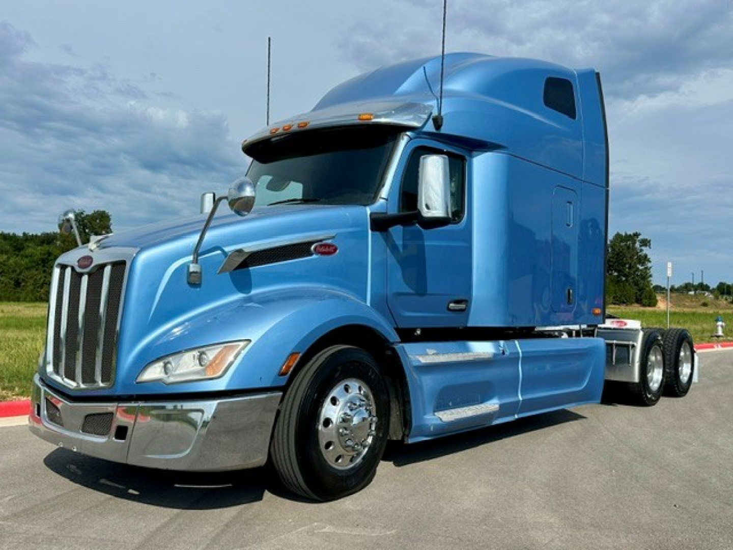 Peterbilt 579 tractor in blue, side view, with sleeper cab and chrome front bumper.