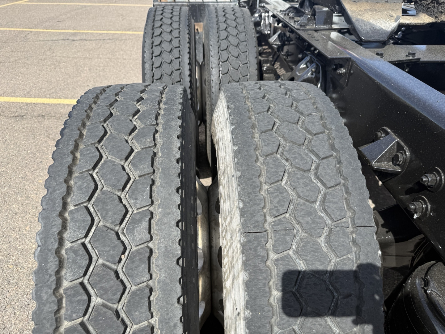 Kenworth T880 axle area showing dual rear axles with treaded truck tires and chassis components.