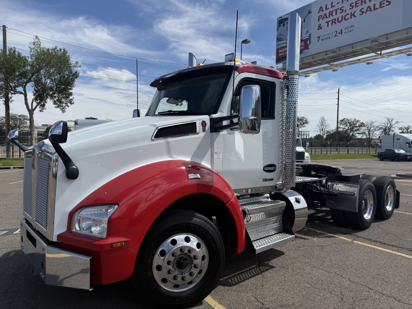 Kenworth T880 conventional daycab truck in white and red, front-left view, with dual rear axles and chrome steps. Road sign in background.