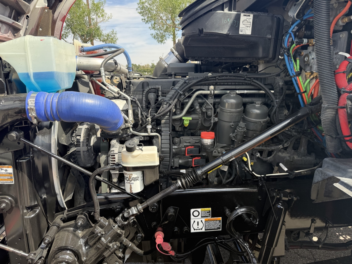 Kenworth T880 engine bay with hoses, reservoir, and wiring harness visible under open hood; labels and caps visible.