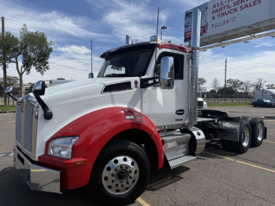 Kenworth T880 conventional daycab truck in white and red, front-left view, with dual rear axles and chrome steps. Road sign in background.
