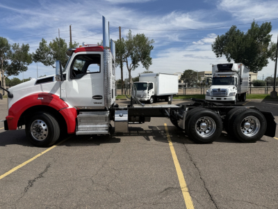 Kenworth T880 truck side view with red cab and white sleeper, chassis exposed, two rear axles, other trucks in background.