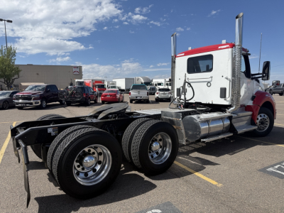 Kenworth T880 cab tractor in a parking lot with dual rear axles and chrome fuel tanks. Side shows no cab interior text but the truck has a white cab with red top.