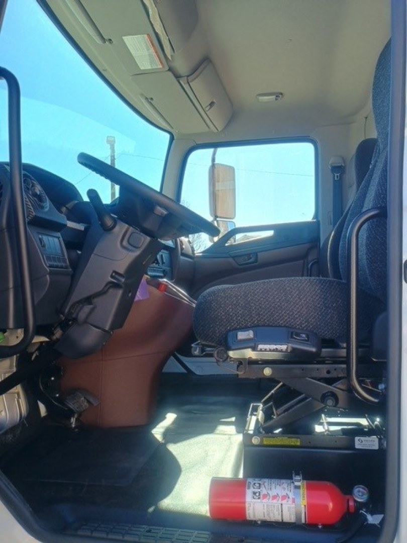 Interior of a new Hino XL8M cab showing steering wheel, driver seat, dashboard, and mounted fire extinguisher in cab. Side door and window visible.