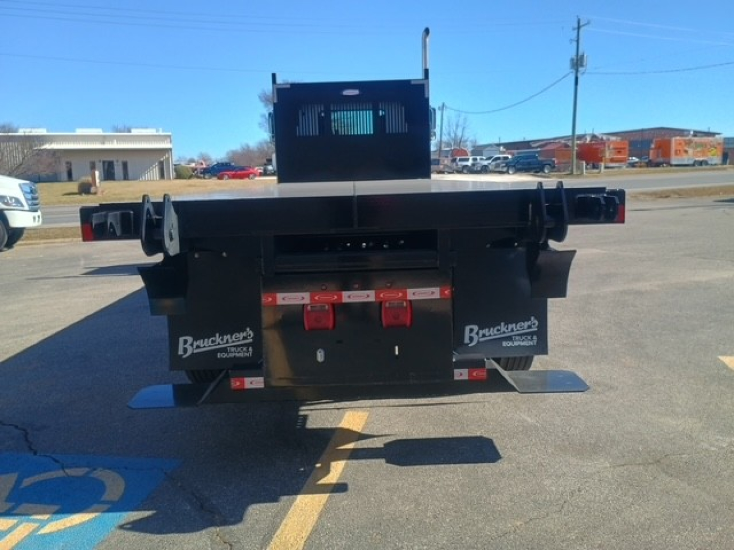 Flatbed truck rear view showing bumper with red hooks and brand labels; warning lights and mud flaps with Bruckner's logo; rear hitch area visible.