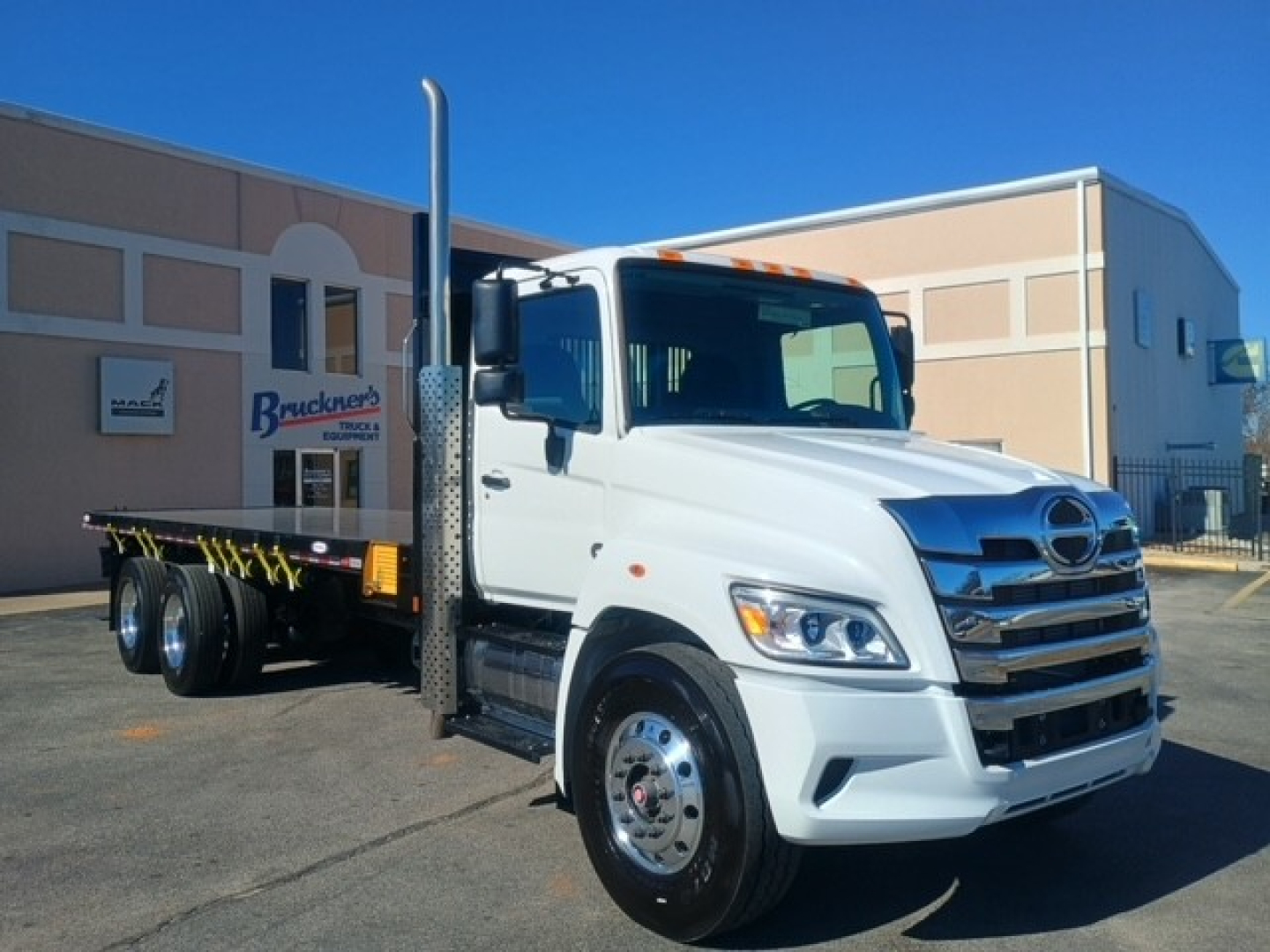 Hino XL8M flatbed truck side view showing front grille, dual rear axles, and tall exhaust stack.