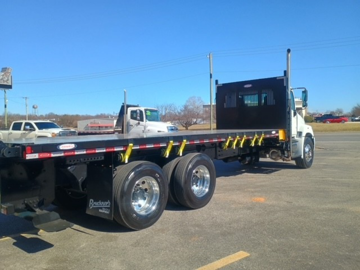 Flatbed truck with dual rear wheels and a high side bed, white cab, long flatbed trailer, Hino XL8M roll-off style truck seen from left-rear angle.