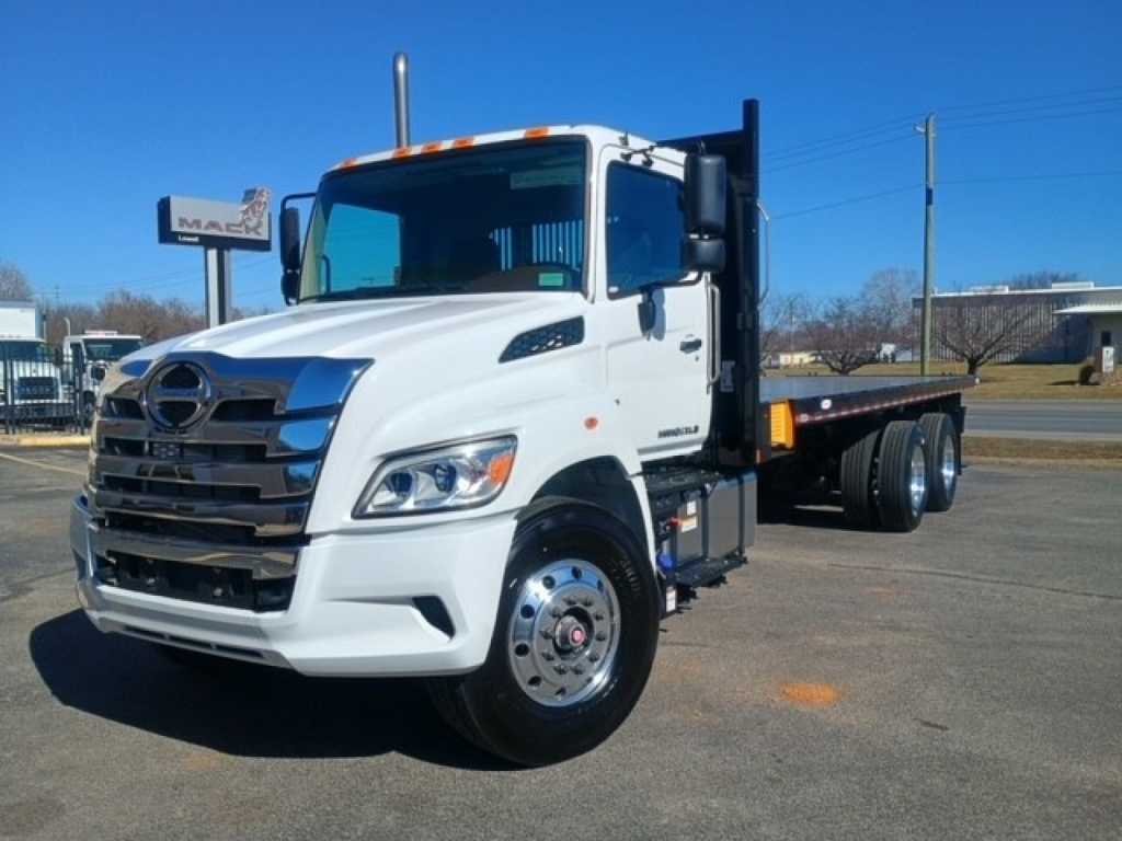 2026 Hino XL8M flatbed truck front-left view showing white cab, chrome grille, and flatbed behind.