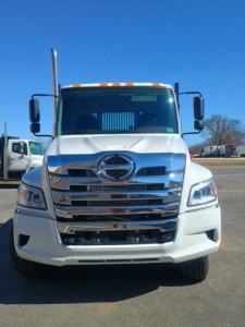 Hino XL8M front view showing chrome grille and S emblem, large windshield, vertical exhaust on left, side mirrors, white cab.