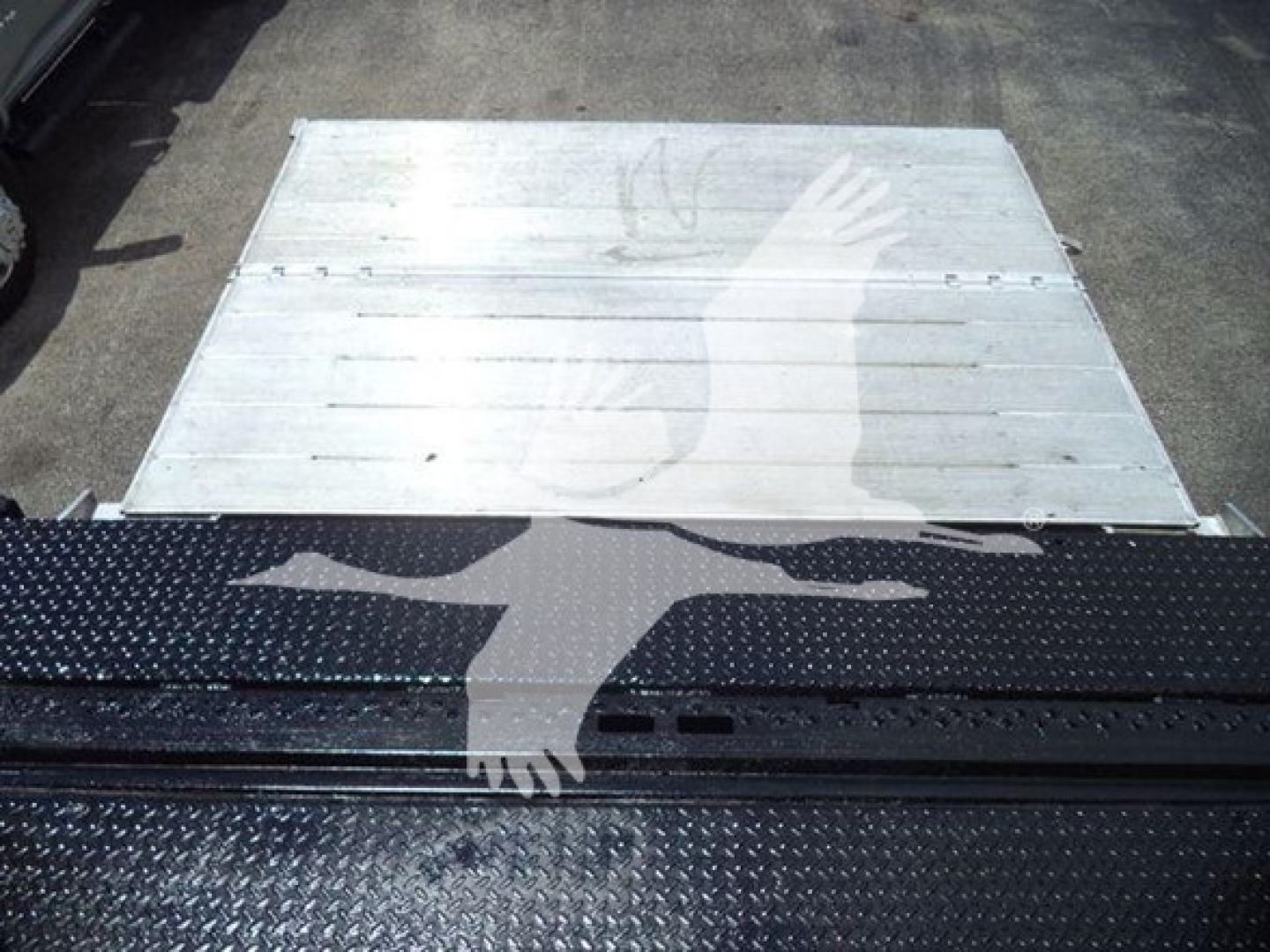 Flatbed or cargo area with metal flooring and a black textured surface featuring a graphic of two hands crossing. No legible model text visible.