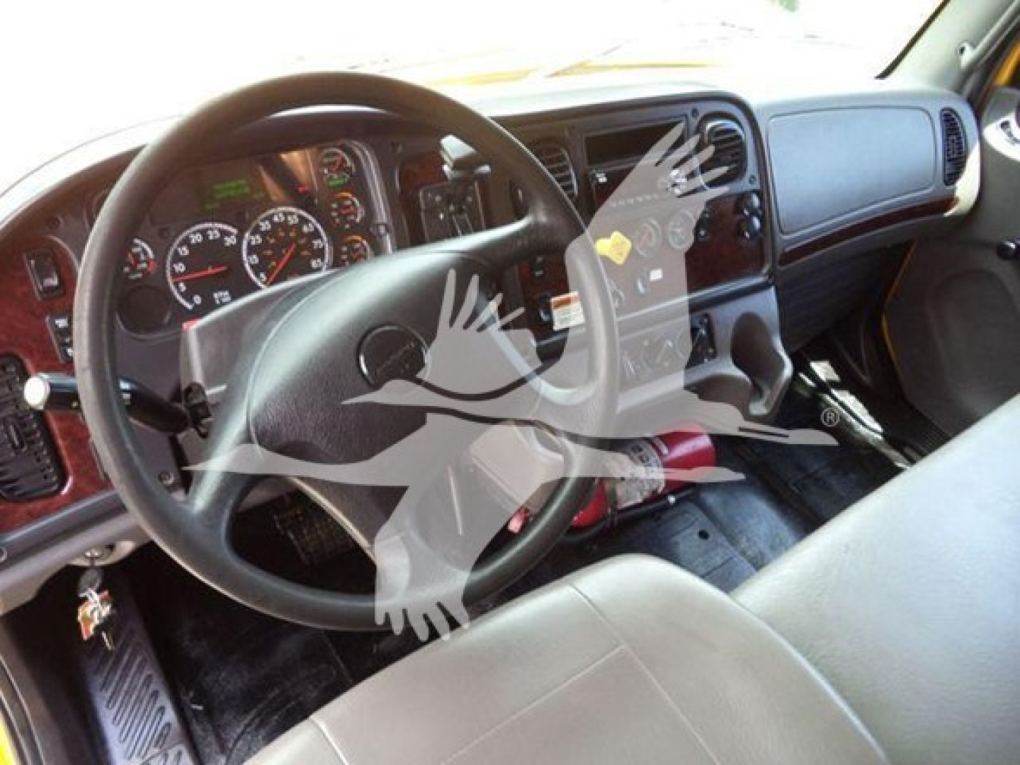 Dashboard and steering wheel of a Freightliner M2 106 commercial truck with a transparent watermark overlay. Visible gauges, steering wheel, center console, and driver seat.