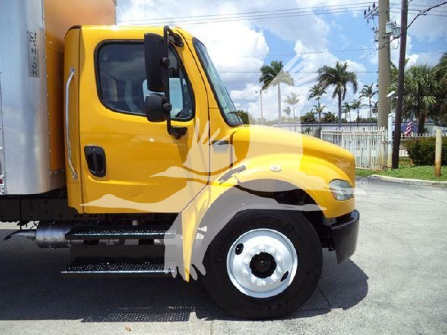 Front left side of a yellow Freightliner M2 106 box truck with chrome steps and black bumper; side window, wheel, and part of cargo box visible.