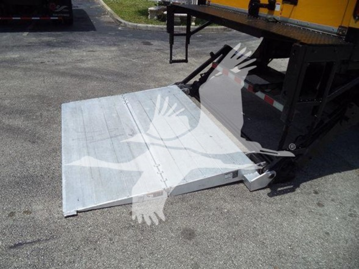 Freightliner M2 106 truck with a lowered aluminum ramp or lift gate in a parking lot, showing the rear platform and hydraulic support arms.