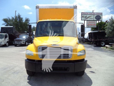 Front view of a yellow Freightliner M2 106 box truck with a large white cargo box, black bumper, and side mirrors; dealership lot in background.