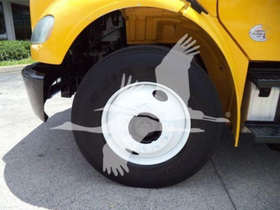 Wheel well of a yellow Freightliner M2 106 truck showing front wheel with white rim and tire; partial view of fender and badge.