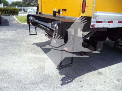Truck rear showing hydraulic lift/boom or underbody cargo equipment on a Freightliner M2 106 with yellow body; tail area and bumper visible.