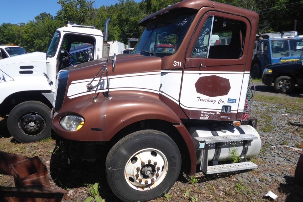 Truck cab close-up showing Freightliner CL112 with brown and white paint and chrome steps.