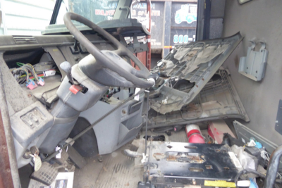 Truck cab interior showing steering wheel dashboard and exposed wiring in a Freightliner CL112 daycab, damaged dashboard panel and exposed components.