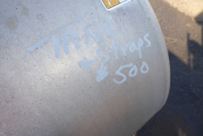 Tank with handwritten white marker text reading 'Trn' and 'straps 500' on grey surface.