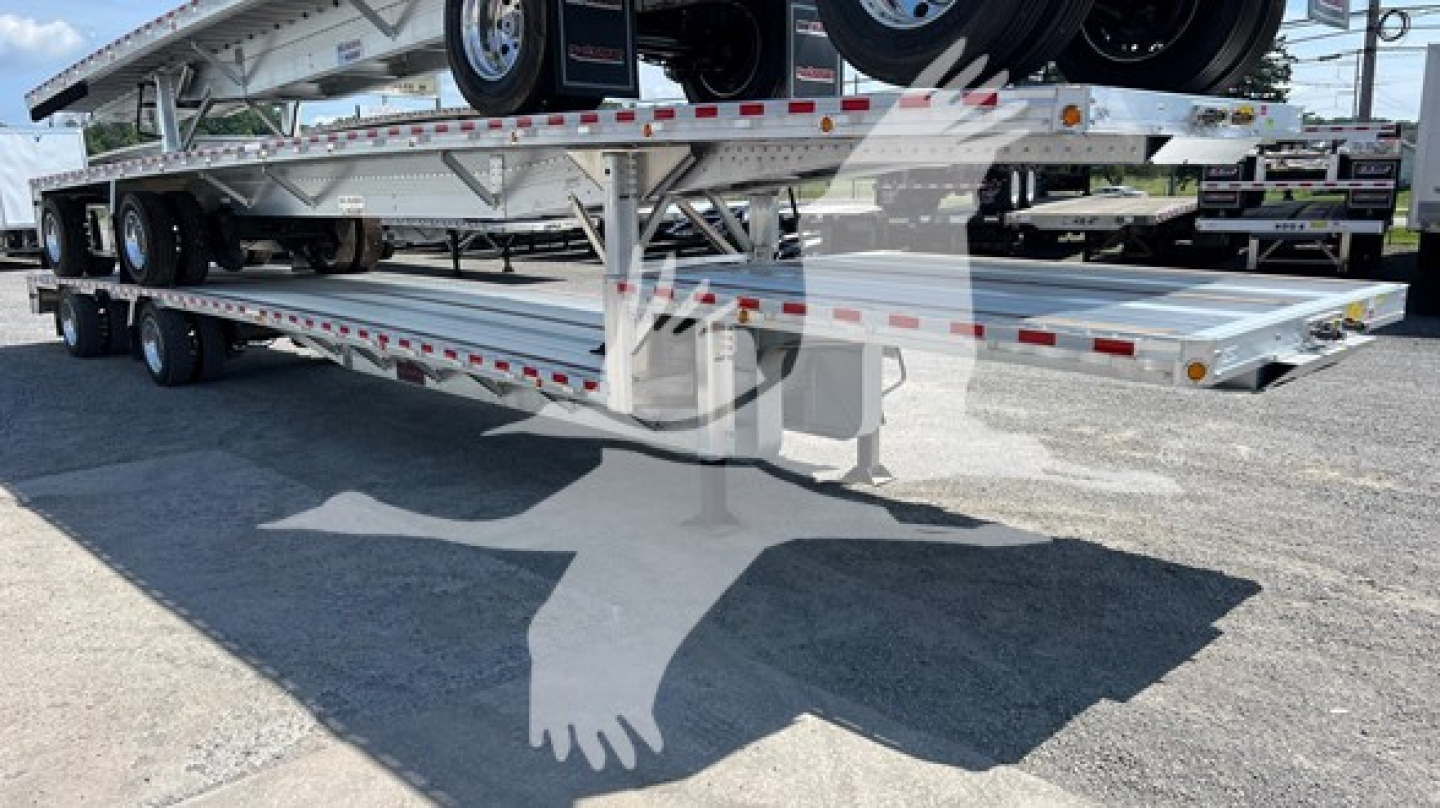 Drop deck trailer showing dual axles and aluminum deck with red/white reflective tape, rear ramps folded, brand: Reitnouer Big Bubba, VIN 1RND53A24TR077231.