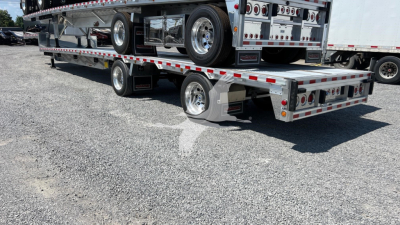 Big Bubba dropdeck trailer with dual-level loading deck and polished aluminum wheels. Side rails and reflective tape visible.