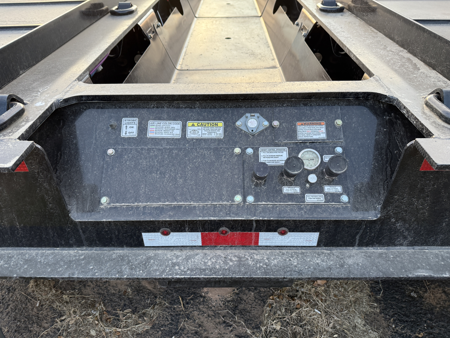 Trailer control panel area showing assorted warning labels, switches, and connectors on Load King trailer rear deck.