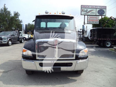 Truck front view of a 2025 Kenworth T280 rollback with chrome grille, dual headlights, and a large windshield; dealership lot in background.