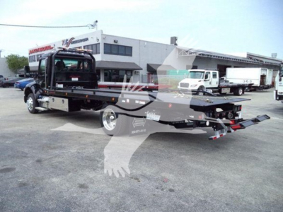 Kenworth T280 rollback truck with flatbed tow bed and distant white service trucks in lot.