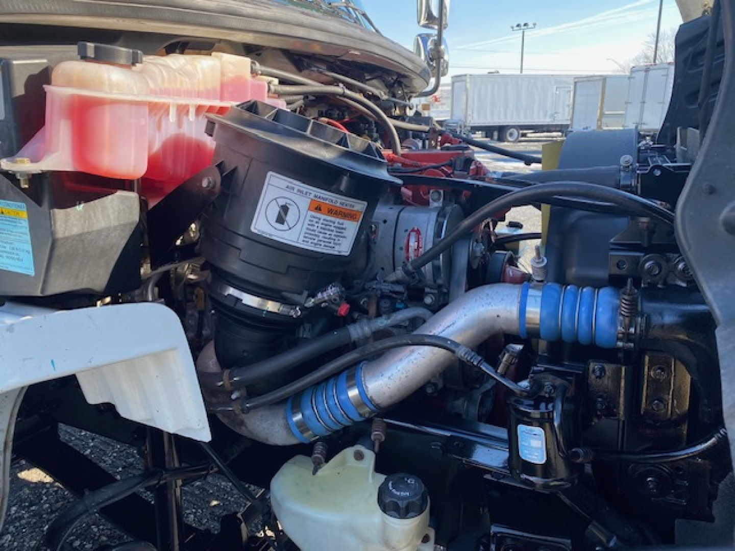 Freightliner M2 106 engine bay showing air intake filter housing, coolant reservoir, blue silicone hoses, and various engine components.