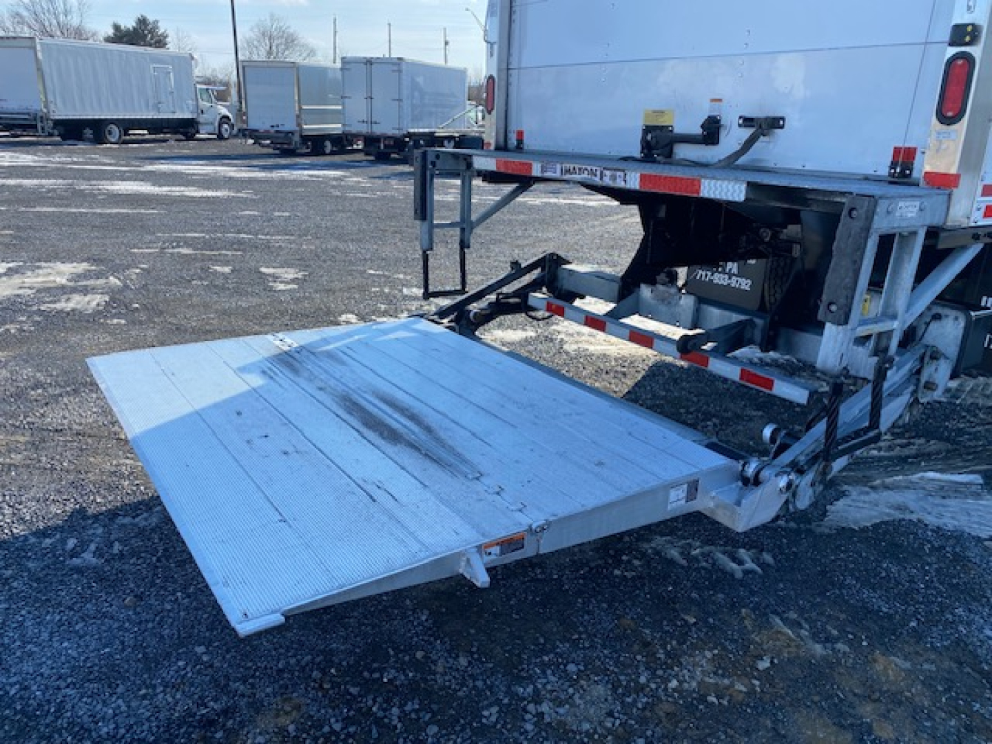 Freightliner M2 106 rear loading ramp extended showing aluminum fold-out lift gate and truck bed with hydraulic mechanism and reflective tape.