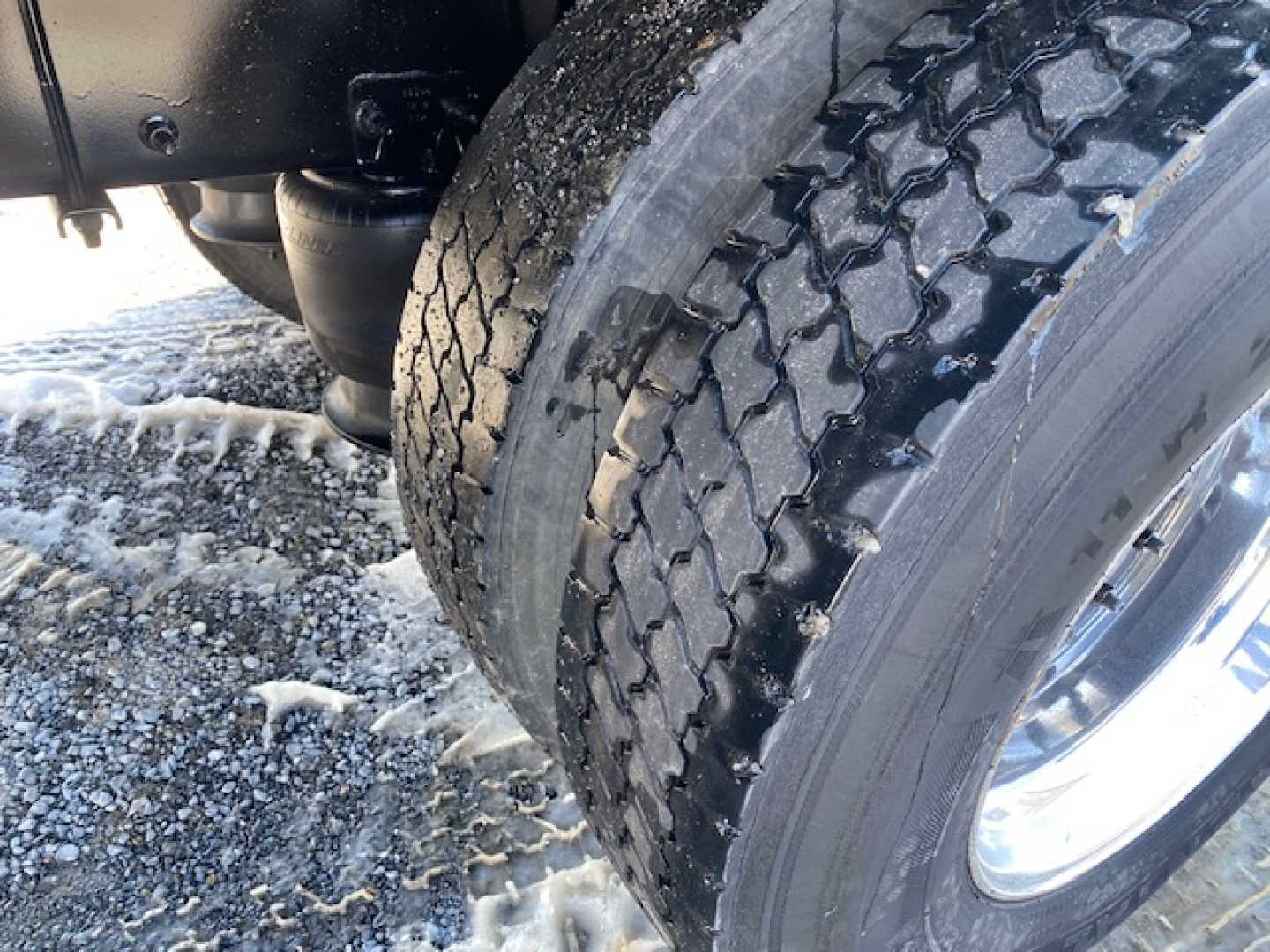 Truck wheel and dual rear tires showing tread pattern and chrome hub, with snow/slush on ground.