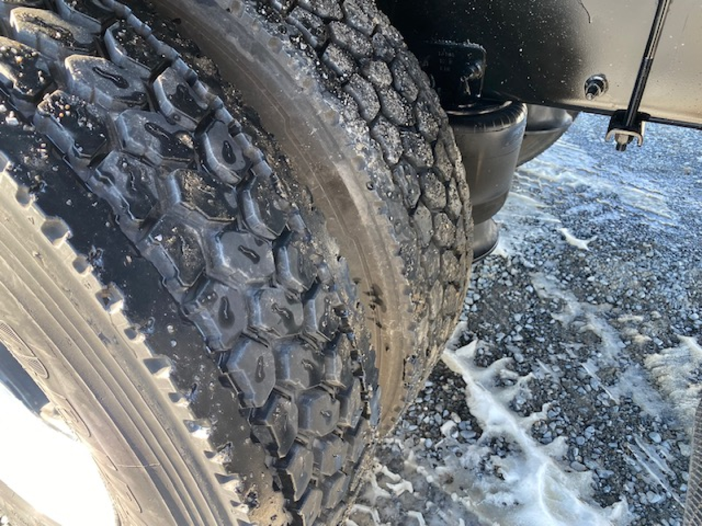 Freightliner M2 106 wheel and tire close-up showing heavy tread and snow on ground.