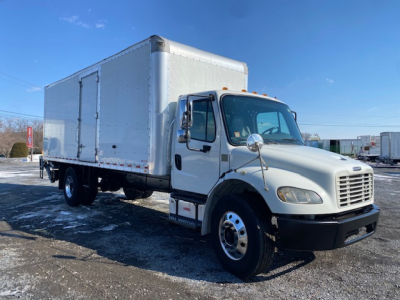 Freightliner M2 106 box truck side/front view showing cab and cargo box with white paint and chrome mirrors.