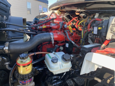 Engine bay of a 2019 Freightliner M2 106 truck showing red engine components, hoses, and a white coolant reservoir
