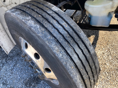 Truck front wheel with dual rear tires visible; exterior shows a white reservoir and some under-hood components.