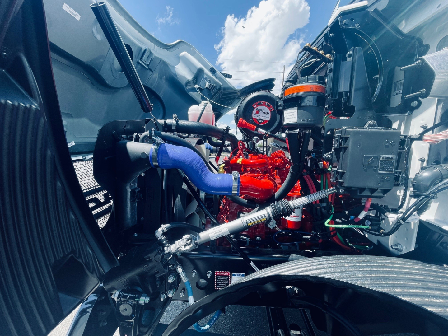 Engine bay of a new 2026 Mack MD6 showing red turbocharger, blue silicone hose, coolant reservoir, and various black wiring looms.